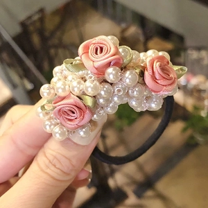 Pink fabric rose and white imitation pearl elastic hair tie held in hand