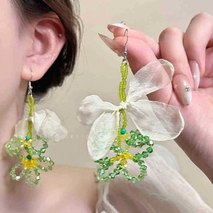 Detail of beaded flower earrings featuring a white fabric bow and soft green beads