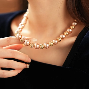 Close-up of elegant champagne pearl and hollow gold bead necklace on a model