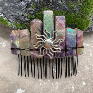 Macro shot of purple crystal hair comb with a silver sun pendant on natural mossy stone