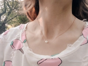 Detailed view of a single white pearl pendant on a thin gold chain worn on the neck