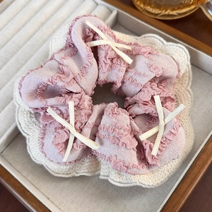 Detailed close-up of pink and beige ruffled scrunchie with delicate bow accents