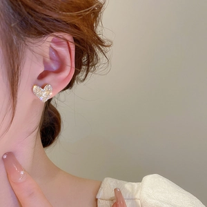 Close-up of a heart-shaped gold earring with crystals worn by a model in warm light