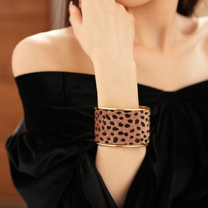 Close-up of wide gold leopard print cuff bracelet worn with a black velvet dress