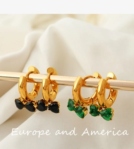 Close-up of gold hoop earrings with black and green heart gemstones on white fabric