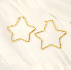 Macro shot of large gold star-shaped hoop earrings on white textured fabric background