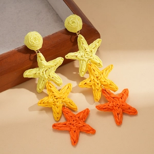 Macro detail of bohemian raffia star tassel earrings in yellow orange and red tones