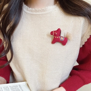 Detail of red fabric horse brooch with embroidery and feather on beige knitwear