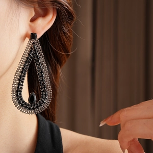 Close-up of black teardrop rhinestone earrings with hollow mesh design worn by a model