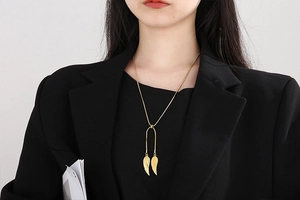 Detail of elegant gold wing pendant on a snake chain worn with a black blazer jacket