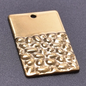 Vue macro d'un pendentif rectangulaire plaqué or 18k avec textures lisses et martelées