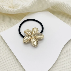 Detail of black hair tie with golden metal flower charm on soft beige fabric background