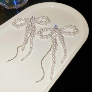 Detailed macro view of bow earrings with hanging pearls and silver tassels on white plate