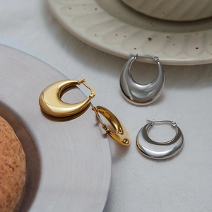 Detailed view of U-shaped gold and silver stainless steel earrings on a fabric background