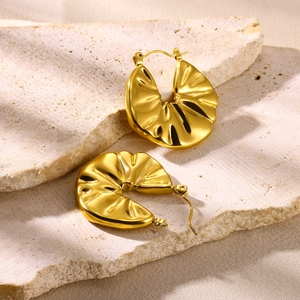 Macro shot of gold-plated hoop earrings with unique wavy wrinkled texture on stone surface