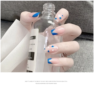 Pink and royal blue press-on nails with heart patterns and French tips held by a hand