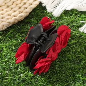 Close-up of velvet red rose flower hair claw clip on a natural green grass background