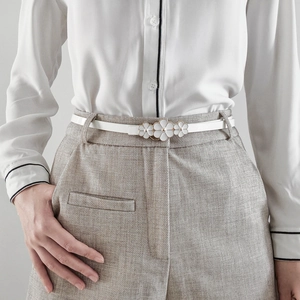 Detail of slim white floral buckle belt worn on beige trousers for elegant styling