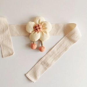 Detail of beige curtain tieback featuring a fabric flower and orange spherical pendants