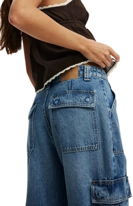 Detail of blue cargo denim jeans showing utility pockets and washed texture on model
