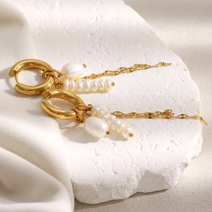 Detailed view of 18K gold plated earrings with pearls on white textured stone
