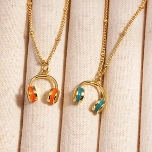 Gold-plated necklace with orange and blue colorful enamel headphone pendant on beige fabric