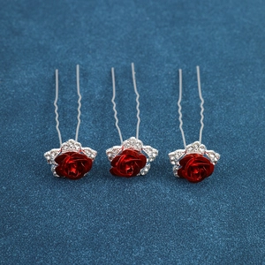 Close-up of three U-shaped bridal hair pins with red metal roses and sparkling rhinestones