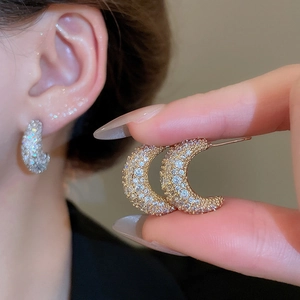 Detailed view of crescent moon stud earrings with white zircons on golden base