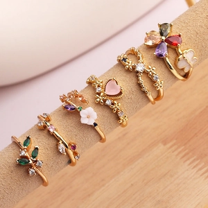 Detail of six gold-plated rings with colorful zircons in heart and flower designs