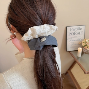 Détail d'un chouchou en dentelle blanche brodée et tissu gris avec accent en métal argent
