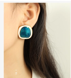 Close-up of irregular geometric earrings with gold trim and teal enamel on a model