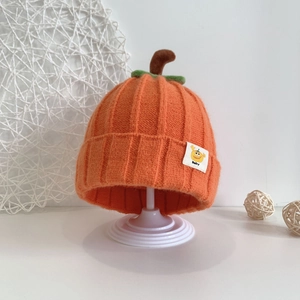 Detailed view of orange pumpkin knit baby hat with green leaf stem and baby label