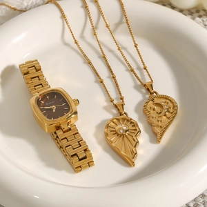 Coffret montre dorée et collier cœur soleil-lune sur un plateau en céramique blanc