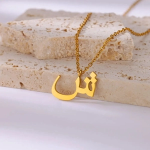 Detailed macro view of a gold stainless steel necklace with Arabic letter Shin pendant