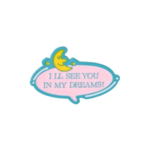 Close-up of pink enamel moon badge with I LL SEE YOU IN MY DREAMS text and stars