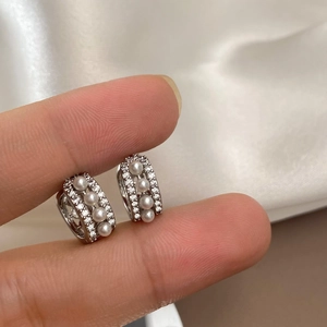 Detailed macro view of U-shaped silver earrings featuring three vertical pearls and pavé zircons