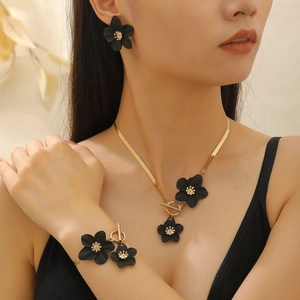 Detail of model wearing a gold necklace and earrings set with black floral pendants