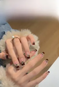 Detail of short burgundy French press-on nails with gold glitter and pearl accents
