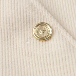 Dettaglio di un bottone in metallo dorato vintage su velluto a coste beige di un cappotto