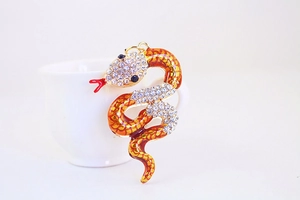 Close-up of sparkling crystal snake charm with red forked tongue on white ceramic edge