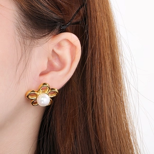 Detailed close-up of golden flower stud earring with pearl inlay worn by a model