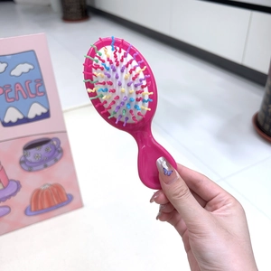 Close-up of a mini massage hairbrush with a rose red body and colorful wavy bristles