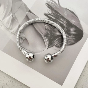 Polished silver twisted rope cuff bracelet with sphere ends on a magazine background