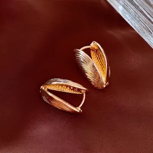 Golden shell-shaped brushed metal hoop earrings displayed on premium brown silk fabric
