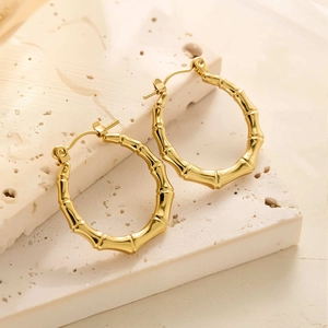 Détail des boucles d'oreilles créoles bambou plaquées or 18k sur une surface en pierre