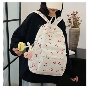 Close-up of cream corduroy backpack featuring red cherry prints and colorful plush charms