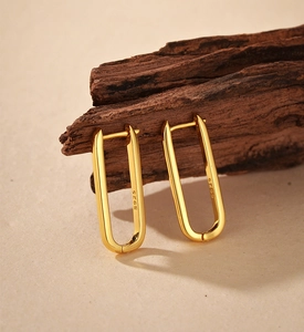 Detailed close-up of golden rectangular S925 sterling silver hoop earrings on wood