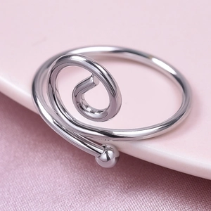 Macro shot of polished silver spiral open ring with metal ball bead on smooth silk fabric