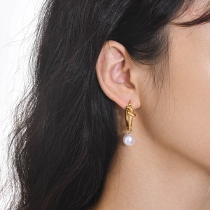Close-up of elegant gold knot earrings with white round pearls on a female model