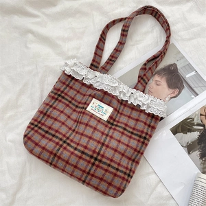 Detailed macro of vintage plaid tote bag with delicate white lace trim and happy patch